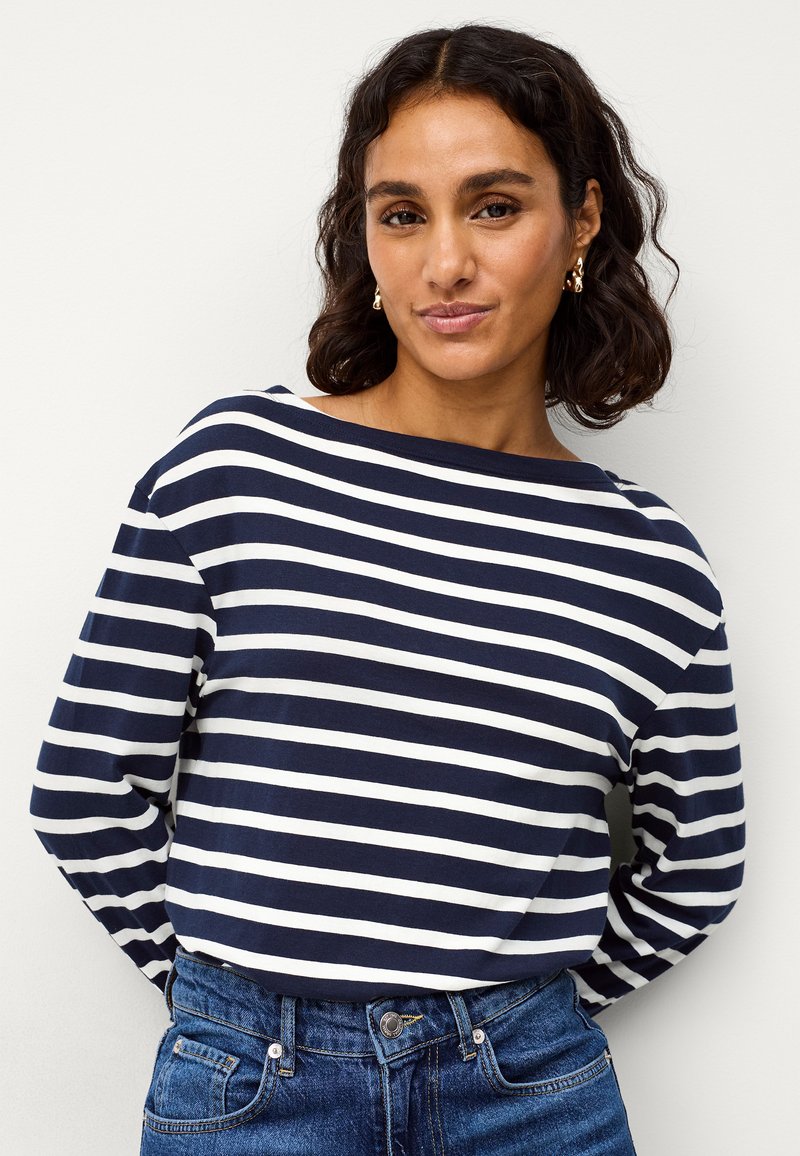 Marineblauwe en witte gestreepte top met lange mouwen en een bootnek, gecombineerd met blauwe denim jeans. De stof lijkt zacht met een comfortabele pasvorm.