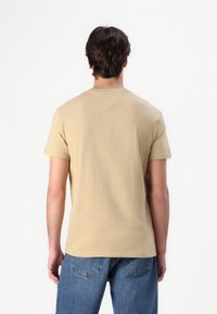 Beige short-sleeve t-shirt with a crew neck, made from a soft cotton blend. Plain back with a clean finish and no visible patterns.