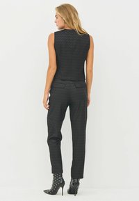 Zwart mouwloos topje en bijpassende broeken van textuurstof, met een aansluitend ontwerp, achterzakken en studded haklaarzen.
