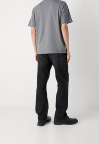 Grijze katoenen t-shirt en zwarte spijkerbroek. T-shirt heeft een relaxte pasvorm; jeans zijn recht toegeknipt met zij- en achterzakken. Zwarte schoenen.