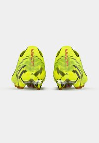 Żółte korki piłkarskie z teksturowanym wzorem, o niskim profilu, z czarnymi akcentami i kolcami zapewniającymi przyczepność. Napis "ULTRA" na pięcie.