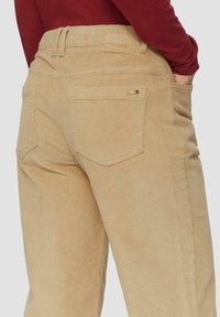 Beige corduroy broek met een ribbeltextuur, voorzien van twee achterzakken en een klein decoratief hardware detail op de tailleband.