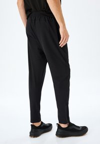 Pantalones deportivos negros con ajuste ajustado, cinturilla elástica y detalles de cremalleras en los laterales. Llevados con zapatillas negras que cuentan con acentos texturizados.
