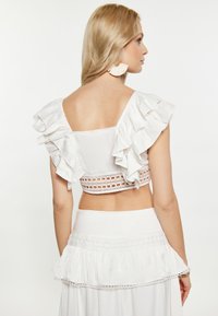 Fehér crop top fodros ujjakkal, nyitott hátsó résszel és csipkés díszítéssel az alján. Puha anyag, könnyű kialakítás, ami alkalmas meleg időjárásra.