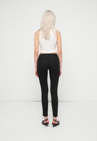 Fekete, magas derekú skinny farmernadrág sima textúrával, hátsó zsebekkel. Egy fehér, rövid topot és fekete magassarkút visel.