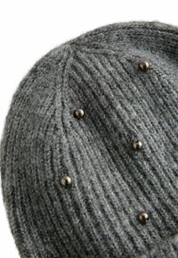 Bonnet en tricot gris en laine, avec une texture côtelée et des clous décoratifs en métal. Le design a une coupe ajustée et un sommet arrondi.