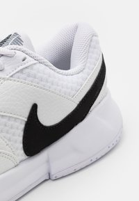 Hvit sportssko med en svart swoosh, teksturert stoff, skinnakenter, polstret krage og hvit gummisåle med synlige dekk.