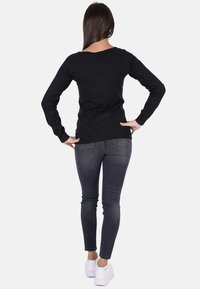 Maglietta nera a maniche lunghe con un design aderente, abbinata a jeans skinny scuri e sneakers bianche. Il tessuto appare liscio e morbido.