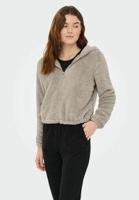 Sweat à capuche zippé gris clair, doux et duveteux, avec capuche et manches longues, assorti à un pantalon noir à taille élastique. Caractérisé par une texture douce.