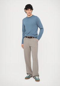 Šviesiai mėlynas megztinis be apykaklės, smėlio spalvos klostuotos kelnės, pasižyminčios lygiu audiniu; derinamos su žaliais sportbačiais su baltais batraiščiais.