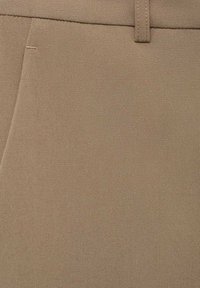 Pantalons beiges sur mesure en tissu lisse, avec un design épuré, une taille plate et un éclat subtil. Détails de couture le long de la taille.