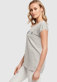 Šedé bavlněné tričko s krátkými rukávy s ohrnutím, na přední straně s černým potiskem nápisu "bloom". Jednoduchý, neformální design.