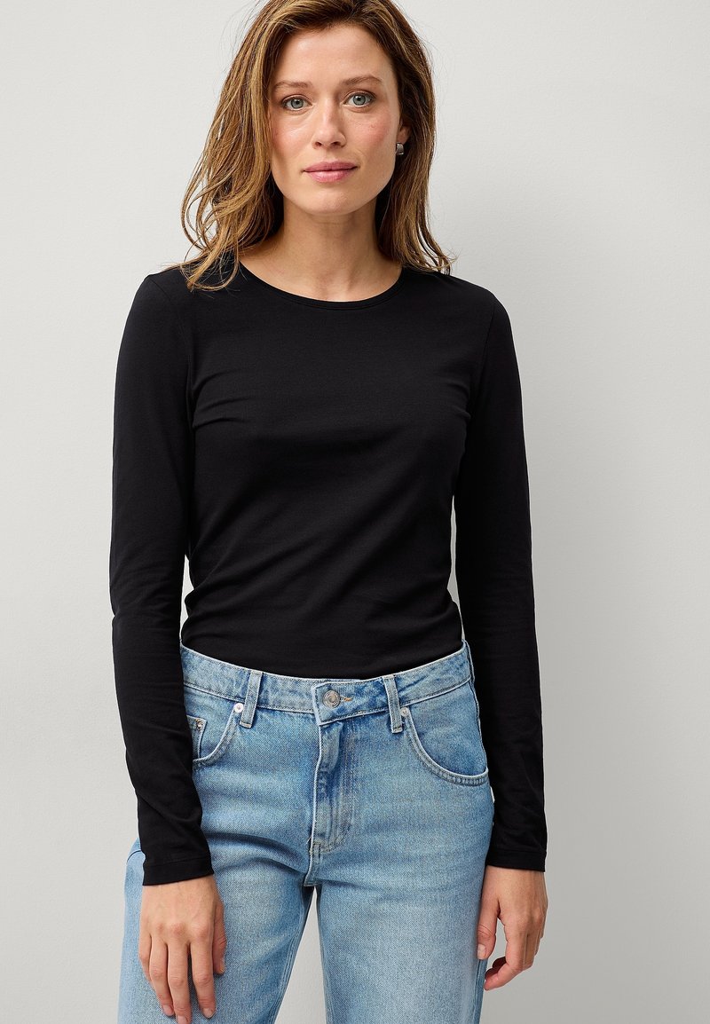 Sort langærmet top med rund halsudskæring, parret med lyseblå højtaljede jeans. Glat bomuldsstruktur, tætsiddende design.