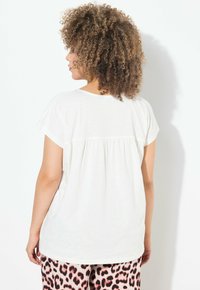 Top blanco de manga corta con un detalle recogido en la parte posterior, combinado con pantalones estampados de leopardo en rosa y negro. Textura de tela suave.