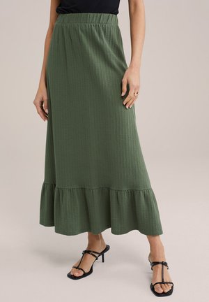 Jupe maxi vert olive en tissu texturé avec une taille élastique, dotée d'un ourlet à volants et assortie à des sandales à talons noires.