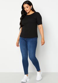 Top corto a righe nere abbinato a jeans skinny blu e sneakers bianche. Il top ha un collo rotondo e aperture laterali.