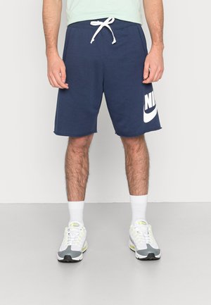 Granatowe bawełniane spodenki z białym logo Nike, elastycznym pasem ze sznurkiem i bocznymi kieszeniami, noszone z białymi skarpetkami do kostek i trampkami.