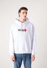 Felpa bianca con cappuccio e tasca a marsupio frontale, con la scritta "HUG" in nero e un grafico di cuore rosso. Maniche e orlo a costine.