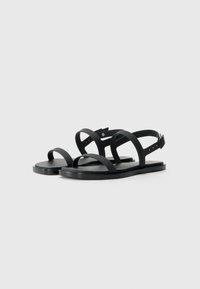 Black sandals featuring a minimalist design with multiple flat straps, a textured sole, and an adjustable ankle strap for secure fit.