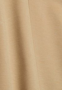 Tissu beige avec une texture tissée fine, montrant une couture verticale visible et de légers plis dans le matériau.