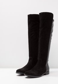 Botas negras hasta la rodilla que combinan ante y cuero liso, con punta redonda y suela plana para mayor estabilidad.