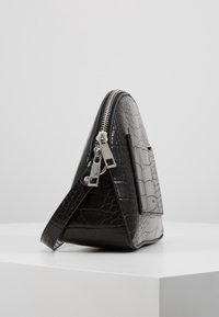 Borsa negras in pelle a stampa di coccodrillo con forma triangolare, con chiusura zip in argento e tracolla removibile. Texture liscia con finitura lucida.