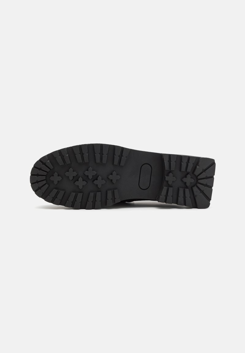 Semelle de chaussure en caoutchouc noir avec des crampons profonds, une découpe ovale et une surface texturée pour une meilleure adhérence. Les accents comprennent des motifs en relief et des indentations.