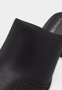 Chaussure noire à enfiler avec tige en cuir lisse et coutures visibles au niveau de la zone des orteils, sur fond blanc.