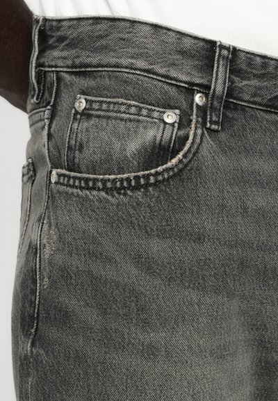 Jeans din denim gri cu o textură uzată, având un design cu cinci buzunare și accesorii metalice. Talie solidă și înaltă.