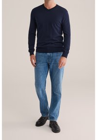 Tmavě modrý svetr s výstřihem do V z měkké látky, spojený s světle modrými džíny se rovnými nohavicemi. Černé boty doplňují outfit.