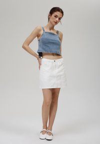 Denim usnjeni top s nastavljivimi naramnicami in surovim robom, v kombinaciji z belo usnjeno mini krilo, ki ima sprednji gumb in žepke.