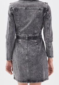 Robe en denim noir délavé, avec manches longues, taille ceinturée et détails de surpiqûres. Présente une coupe ajustée et une longueur au-dessus du genou.