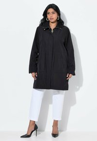 Svart vattentät jacka med dragkedja, två framfickor och krage. Bärs med vita korta byxor och svarta klackar.