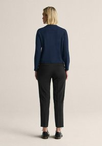 Marinblå stickad kardigan med långa ärmar och rund halsringning, ihop med svarta snäva byxor och svarta snörskor. Enkel, strukturerad design.