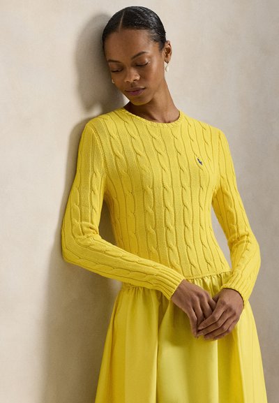 Κίτρινο πλεκτό πουλόβερ με σχέδια κοτσίδας και μακριά μανίκια, σε συνδυασμό με μια ταιριαστή κίτρινη φούστα. Λείο υφάσμα και στρογγυλή λαιμόκοψη.