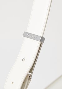 Bijela kožna remen s srebrnim hardverom, s Calvin Klein logom i detaljima u šavovima. Glatka tekstura i ravni dizajn.
