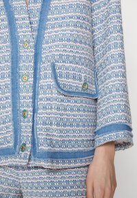 Veste tissée bleu clair et rose avec pantalon assorti, boutons dorés, bordure texturée et poche à rabat sur le devant de la veste.