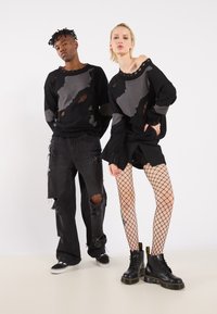 Zwarte en grijze truien met versleten patronen, gecombineerd met gescheurde zwarte broeken en shorts, netpanty's en zwarte combatboots.