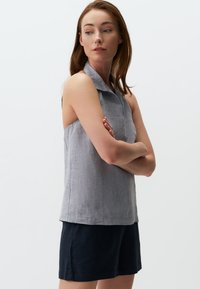 Top senza maniche in lino grigio con colletto; abbinato a pantaloni corti blu navy. Il tessuto ha una leggera trama e una vestibilità ampia.