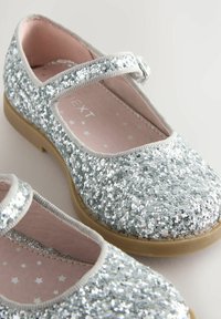 Scarpe Mary Jane argentate glitterate con punta tondeggiante, una fascia in tessuto e una suola in gomma beige; foderate con materiale a fantasia di stelle rosa.