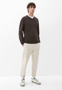 Brauner V-Ausschnitt-Pullover und hellbeige Hose, kombiniert mit weißen Sneakern. Das Outfit zeichnet sich durch eine lockere Passform und ein lässiges Design aus.