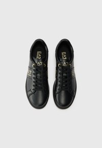 Sorte lærersneakers med rund tå, flade snørebånd, guldfarvede detaljer og logo på siden og indersålen. Glat tekstur og elegant design.