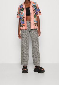 Camisa rosa de manga corta bordada con flores, combinada con pantalones anchos de cintura alta en blanco y negro con un patrón, complementada con sandalias negras de plataforma.