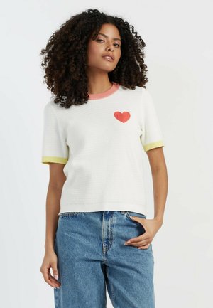 Weißes Strick-T-Shirt mit kurzen Ärmeln, pinken und gelben gerippten Bündchen, mit einem roten Herz-Logo auf der linken Seite.