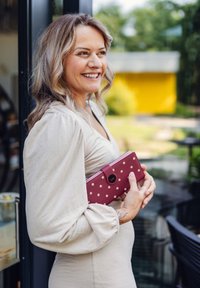 Polka-dot burgundy wallet with a clasp closure held against a light beige dress; soft fabric and defined silhouette visible.