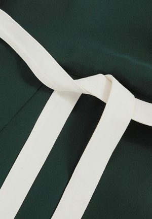 Roheline kangas, millel on sile tekstuur, on kaunistatud valge vööga, mis on seotud paelaga, tuues esile rõiva disainielemendid ja kontrastsed värvid.