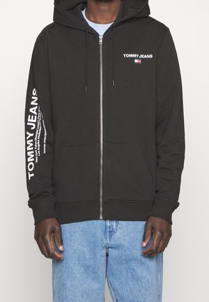 Zwarte hoodie met rits, voorzakken en een capuchon met trekkoord. Heeft witte tekst en logo "TOMMY JEANS" op de borst en mouw.