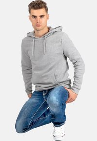 Grijze katoenen hoodie met een trekkoordcapuchon en een kangoeroezak, gecombineerd met blauwe jeans met een versleten textuur en witte sneakers.