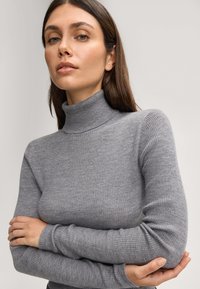 Maglione grigio a collo alto con coste, maniche lunghe, texture liscia e design aderente. Presenta un collo alto e polsini aderenti.