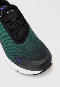 Žalios ir juodos sportinės bateliai su tinkline viršutine dalimi, tekstūruotais elementais, juodais raišteliais ir mėlynu Nike logotipu. Balta padas su akcentu ant kulno.